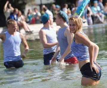 Woman wearing a blue-and-white telnyashka celebrating Airborne Forces Day with VDV veterans in a city fountain.